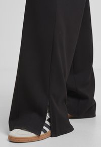 Fekete, bő szárú nadrág, amelynek alján hasítékok találhatóak, feket és fehér csíkos fehér sportcipővel és gumi talppal. Simává szövettextúra.