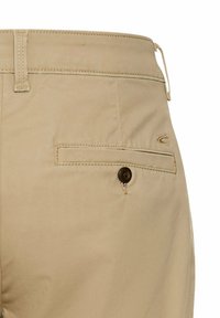 Beige cotton pants featuring a back pocket with a brown button closure. Stitch detailing along the pocket and waistband.