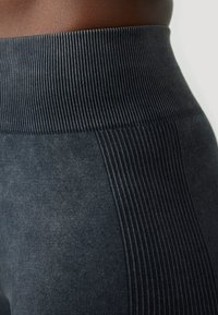 Uski blizu tamno sivi bezšavni tajice s rebrastim visokim pojasom oko struka i bokova osobe.