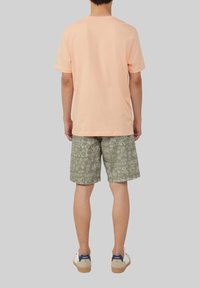 Lichtroze katoenen T-shirt gecombineerd met groene gestreepte shorts met een bloemdessin, afgemaakt met beige en marineblauwe sneakers.