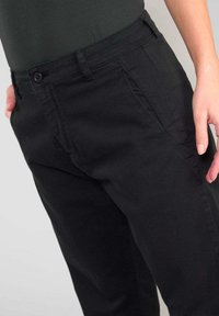 Zwarte katoenen broek met een knoopsluiting, zijzakken en een recht model. De stof heeft een gladde textuur en minimale stiksels.