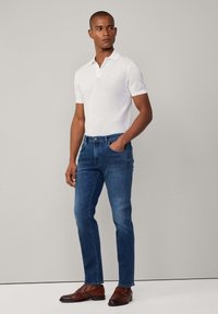 Weißes kurzärmeliges Poloshirt, blaue enganliegende Jeans und braune Lederschuhe. Einfaches Design mit einem Kragen und dezentem Branding. Glatte Textur.