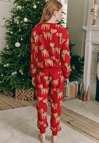 Rode pyjamastel met een herhaald rendierpatroon in beige en blauw. Zacht materiaal met geribde manchetten en tailleband. Losse pasvorm, enkel-lang.