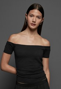 Top nero senza spalle realizzato in tessuto texturizzato, con maniche corte e design aderente, caratterizzato da sottili motivi orizzontali.