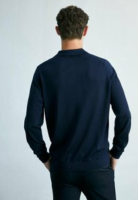 Pull en maille bleu marine avec col, manches longues et ourlet côtelé. Texture lisse, design simple, vu de l'arrière.