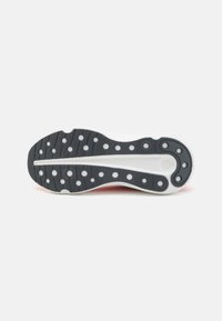 Semelle en caoutchouc noir avec des motifs de traction circulaires et ovales blancs, design texturé, et un accent rose au talon.