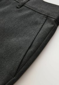 Pantalon en laine gris foncé avec un gros plan sur la couture latérale et les détails de la ceinture sur un fond blanc.