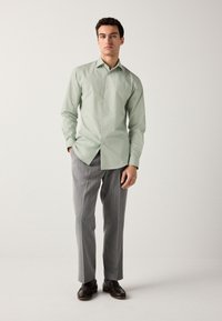 Lysegrøn langærmet skjorte med knaplukning, kombineret med grå bukser med nålestriber og brune lædersko.