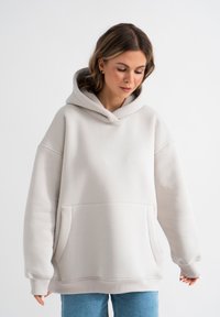 Overmaatse lichtgrijze hoodie gemaakt van zacht materiaal, met een grote voorzak, ribbelmanchetten en een ruime capuchon.