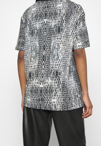 Koszula z krótkim rękawem w czarno-białym wzórze węża. Okrągły dekolt, luźny krój, lekki materiał i gładka tekstura.