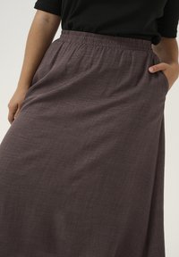 Fustă lungă, cu talie elastică, fabricată dintr-un material texturat și ușor, de culoare prune închis. Are buzunare laterale și o siluetă netedă.