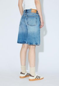Shorts en denim de couleur bleu clair avec un lavage délavé, dotés d'une taille standard, de deux poches arrière et de détails à ourlet brut. Étiquette tan à l'arrière.