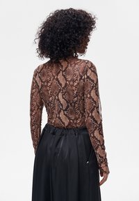 Brązowa bluzka w wężowy wzór z długimi rękawami, o dopasowanym kroju. Połączona z czarną satynową spódnicą z wysokim stanem.