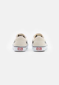 Cream-colored suede and canvas sneakers with black stripes and white soles, featuring a red Vans logo at the heel.