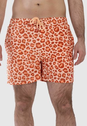 Mann trägt orange- und pfirsichfarbene Badehose mit Leopardenmuster und vorderer Schnürung, steht mit entspannten Armen an den Seiten.