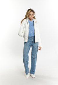 Hvid pufferjakke med lynlåslommer, blå strikket sweater og lyseblå denim jeans. modellen bærer hvide sneakers. Simpelt, funktionelt design.