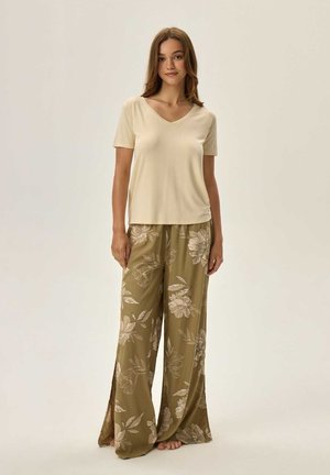Beige V-Ausschnitt Kurzarmoberteil kombiniert mit olivgrünen, weit geschnittenen Hosen mit floralem Muster und seitlichen Schlitzen für zusätzlichen Detailreichtum.