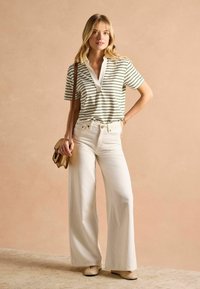 Ribadeega polo särg valge kraega, kombineeritud laiade valgete pükstega. Aksessuaaride hulka kuulub väike pruun käekott. Sujuv, mugav disain.