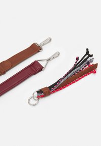 Due portachiavi multicolori: uno con una cinghia in pelle marrone dotata di clip argentate e l'altro con una cinghia in tessuto intrecciato nei colori rosso, nero e blu con dettagli decorativi.