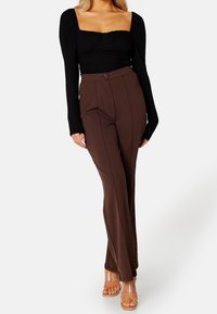 Top nero a maniche lunghe con scollatura quadrata abbinato a pantaloni high-waisted marroni con bottone frontale e cuciture verticali. Tacchi trasparenti.