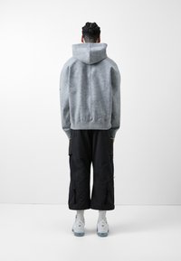 Grå hettegenser med teksturert finish, kombinert med svarte cargo-bukser og hvite sneakers. Antrekket er sett fra baksiden.