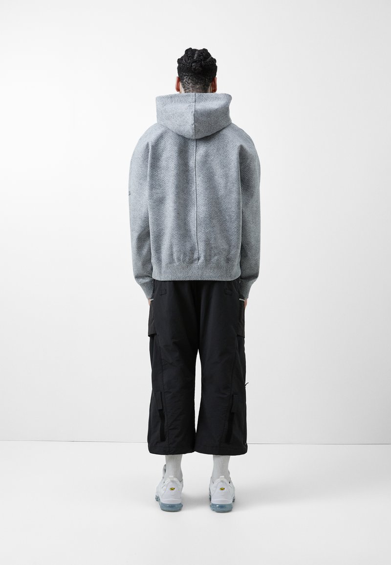 Szary sweatshirt z kapturem o teksturowanym wykończeniu, w połączeniu z czarnymi spodniami cargo i białymi sneakersami. Strój widoczny z tyłu.