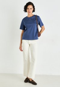 Navyblauwe top met korte mouwen en ronde hals, gecombineerd met crèmekleurige wijde broek en bruine instappers. Een kleine schoudertas voegt detail toe.