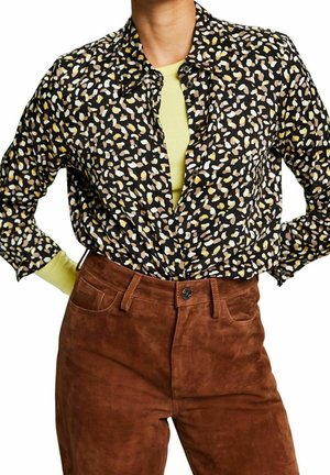 Camicia nera con un motivo astratto colorato, dotata di colletto e bottoni, abbinata a pantaloni in suede marrone. Tessuto testurizzato visibile.