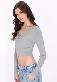 Szürke, bordázott, hosszú ujjú cropped top V-nyakkivágással, középen ráncolt részlettel, amelyet magas derekú farmer sorttal párosítottak.
