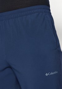 Pantalons de sport bleu marine, en tissu léger, avec une taille élastique et un petit logo Columbia sur la jambe inférieure.