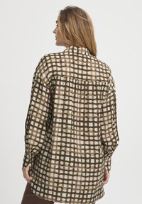 Chemise à carreaux marron avec des motifs verts et crème, à manches longues, coupe ample et détail en empiècement dans le dos. Tissu doux et léger.