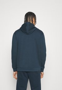 Felpa con cappuccio di colore blu navy, dalla vestibilità rilassata, texture morbida e polsini e orlo a costine. Presenta un piccolo logo in basso a sinistra.