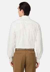 Camicia bianca a maniche lunghe con sottili righe verticali, polsi con bottoni e colletto a punta. Indossata con pantaloni marroni e una cintura intrecciata.