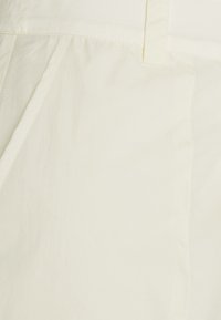 Lichtroomkleurige stof met een gladde textuur en een lichte glans. Kenmerkt zich door schone stiksels en een klassieke, op maat gemaakte snit.