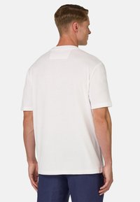 Bílá tričko s krátkým rukávem a texturovaným povrchem. Na zadní straně se nachází malá čtvercová nášivka na krku. Jednoduchý a minimalistický design.