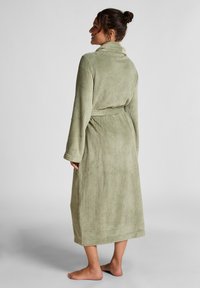 Lang grønn badekåpe i waffle-strikk med sjalkrage, belte med knyting og lange ermer, med en teksturert overflate og lengde til midten av leggen.