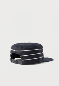 Καπελάκι ναυτικού μπλε χρώματος με επίπεδη γείσο και λευκές οριζόντιες ρίγες, ρυθμιζόμενο πίσω κλείσιμο με πλαστικό κούμπωμα.