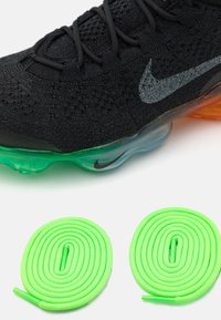 Black athletic shoe with textured knit upper, green and orange air cushion sole, and silver Nike logo; includes two neon green shoelaces.