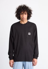 Black long-sleeve t-shirt made of cotton, featuring a chest pocket with a square logo. The design is relaxed-fit with a round neckline.