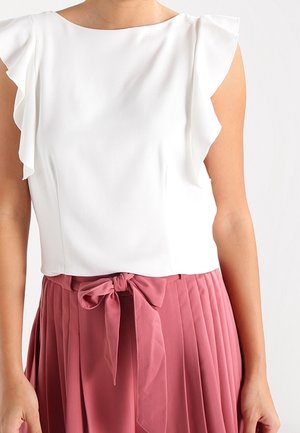Blusa blanca sin mangas con hombros con volantes combinada con falda plisada de talle alto en color rosa polvo, atada con un lazo en la cintura.
