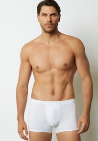 Bílé boxerky vyrobené z měkké tkaniny s přiléhavým designem, vybavené rovnými gumami v pase a plochými švy pro maximální pohodlí.