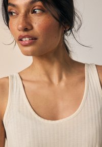 Débardeur beige clair côtelé avec un col en U et des bretelles larges ; présente une texture lisse et un design minimaliste.