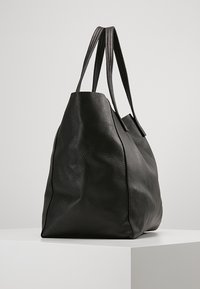 Stor svart toteväska i grängad läder. Har två långa handtag, mjuk textur och en rymlig, avslappnad form. Ingen synlig hårdvara.