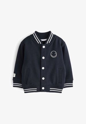 Chaqueta varsity de color azul marino en material suave, con botones blancos, cuello y puños acanalados a rayas, y un detalle de cara sonriente bordado.