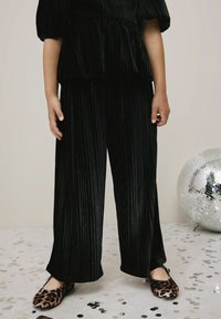 Czarna, plisowana bluzka z weluru i szerokie spodnie w parze z balerinami w leoparda. Błyszczące konfetti rozsypane na podłodze i kula dyskotekowa w pobliżu.