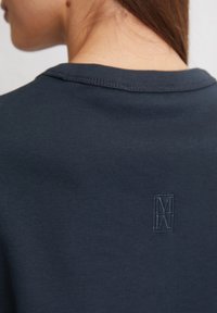 Maglietta a maniche corte blu scuro con colletto a girocollo e logo ricamato discreto sul retro. Tessuto morbido con una finitura liscia.