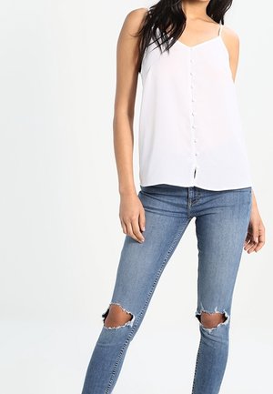 Hvid ærmeløs top med knapdetalje foran, kombineret med lyseblå slidte skinny jeans med frynset kant og knæudskæringer.