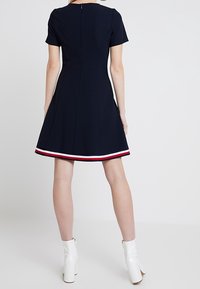 Vestido A-line de color navy con mangas cortas, que presenta un corsé ajustado y un dobladillo acentuado en blanco y rojo. Cierre de cremallera en la parte posterior.
