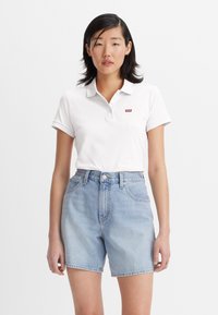 Vit polo-shirt med korta ärmar och en röd Levi's-logga. Matchad med ljusblå denimshorts med hög midja och framfickor.