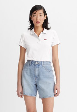 Valkoinen lyhythihainen polo-paita, jossa on punainen Levi's-logo. Yhdistetty vaaleansinsisiin farkkushortseihin, joissa on korkea vyötärö ja etutaskut.